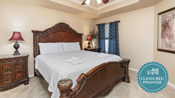 A clean, well-maintained bedroom with a wooden bed, a ceiling fan, and a nightstand with a lamp. - Spacious Family Retreat | Pool Access & Beach Nearby (Corpus Christi)