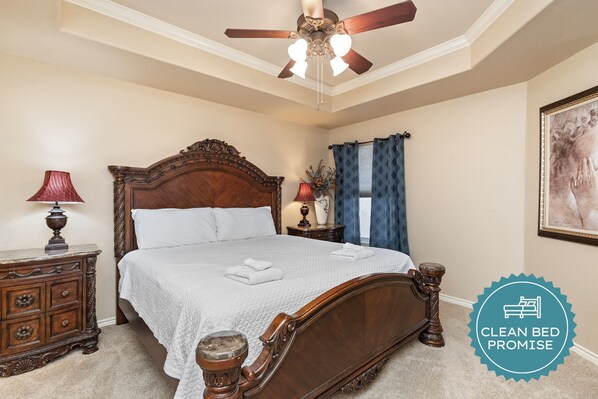 A clean, well-maintained bedroom with a wooden bed, a ceiling fan, and a nightstand with a lamp.