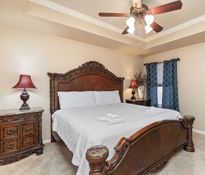 A clean, well-maintained bedroom with a wooden bed, a ceiling fan, and a nightstand with a lamp.