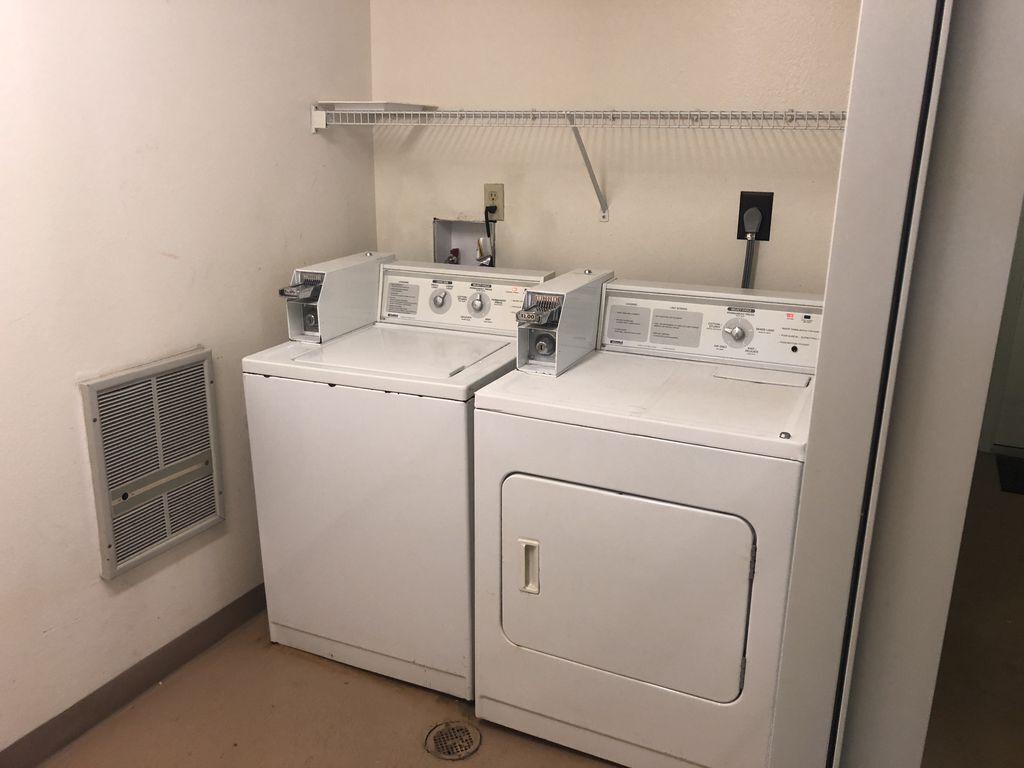A laundry room with two stacked washers and dryers, a vent, and a shelf above the dryers.
