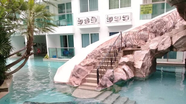 A pool with a rock feature and stairs, surrounded by a building with large windows and a balcony. - Amazon Residence Condo by MaiNot (Pattaya)