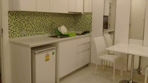 A compact kitchen with white cabinets, a green and white tiled backsplash, a sink, and a small refrigerator. - Amazon Residence Condo by MaiNot (Pattaya)