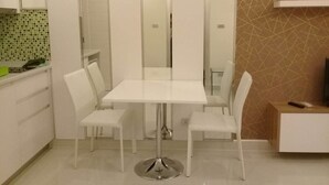 A modern kitchen with white cabinetry, a tiled backsplash, and a dining area with a white table and chairs. - Amazon Residence Condo by MaiNot (Pattaya)