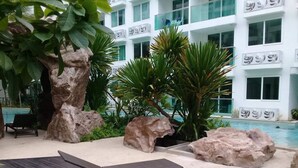 A poolside area with lounge chairs, large rocks, and tropical plants. - Amazon Residence Condo by MaiNot (Pattaya)