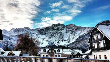 A mountain village with traditional wooden houses, a stone wall, and snow-covered peaks in the background.