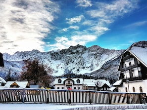 Un village de montagne avec des maisons traditionnelles en bois, un mur de pierre et, en arrière-plan, des sommets enneigés.