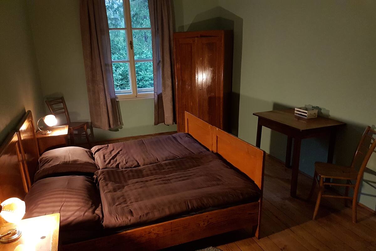 A bedroom with a wooden bed, a desk with a lamp, a chair, and a wardrobe.