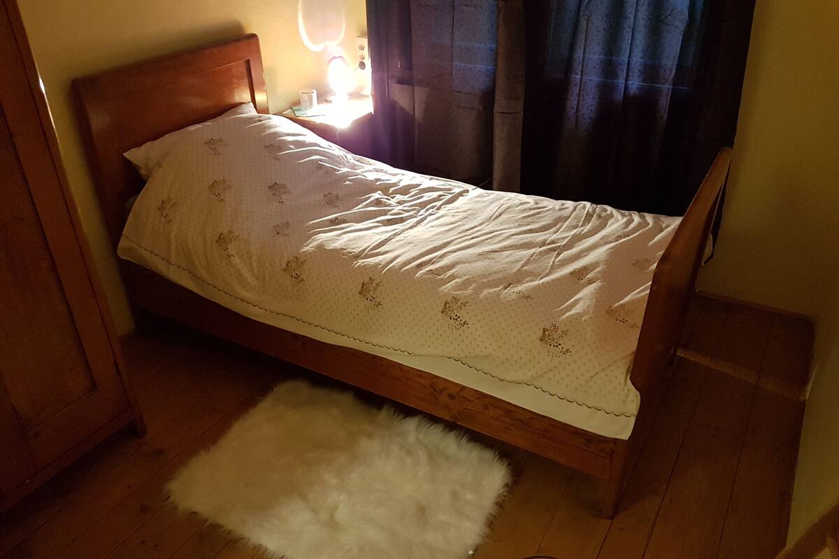 A single bed with a wooden headboard, a white fluffy rug, and a bedside table with a lamp.