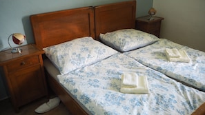 Un lit double avec une literie à motifs floraux, deux oreillers, une tête de lit en bois, une table de chevet avec une lampe et une paire de chaussons.