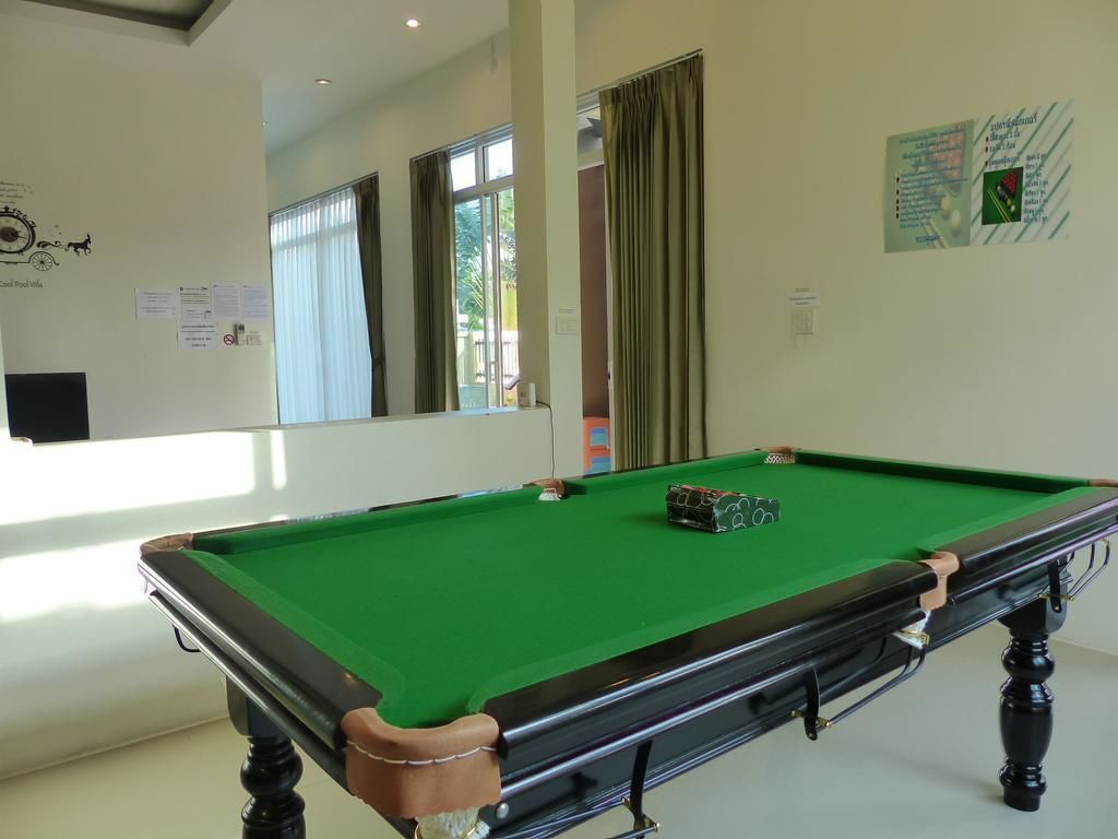 Una mesa de billar en una habitación con un espejo grande, una ventana con cortinas y una pared con carteles informativos.