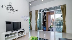 Una sala de estar moderna con un televisor de pantalla plana, un mueble blanco para equipo multimedia y un amplio ventanal que da a un balcón exterior.