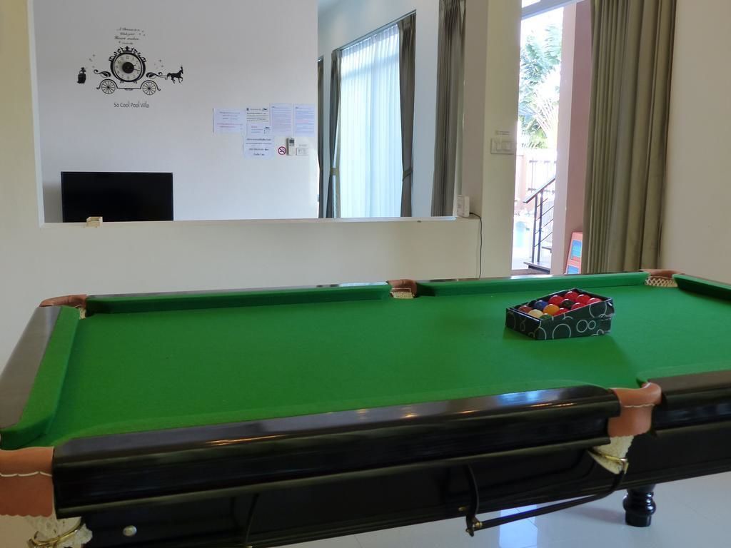 Ein Billardtisch mit Spielball und Kugelset, eine Tafel mit Kompasszeichnung und Beschriftung sowie ein Fenster mit Vorhängen.