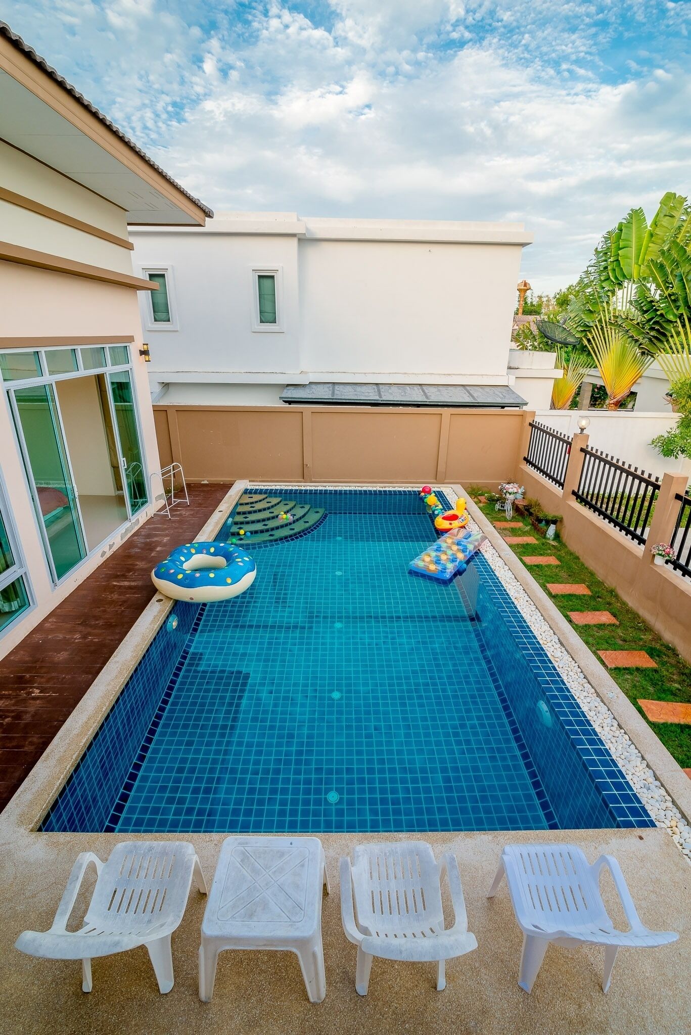A swimming pool with blue tiles, surrounded by white chairs and a lounge area.