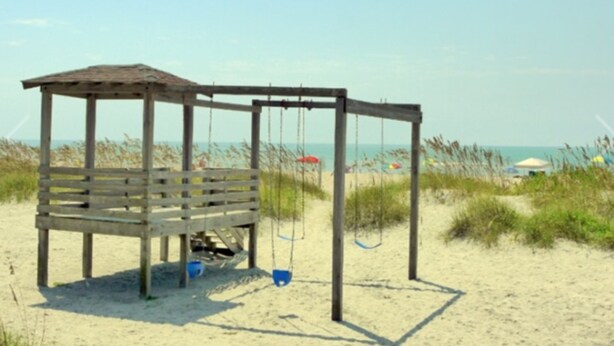 Una estructura de madera en la playa con un banco y columpios.