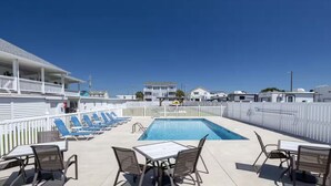 Zona de piscina con sillones y mesas, un cielo azul despejado, y vehículos recreativos al fondo.