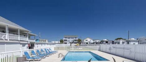 A pool area with lounge chairs and tables, a clear blue sky, and RVs in the background.