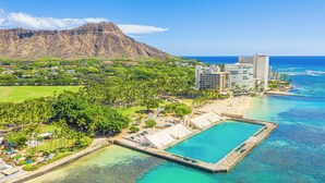 Un resort costero con una gran piscina, villas frente a la playa y montañas al fondo.