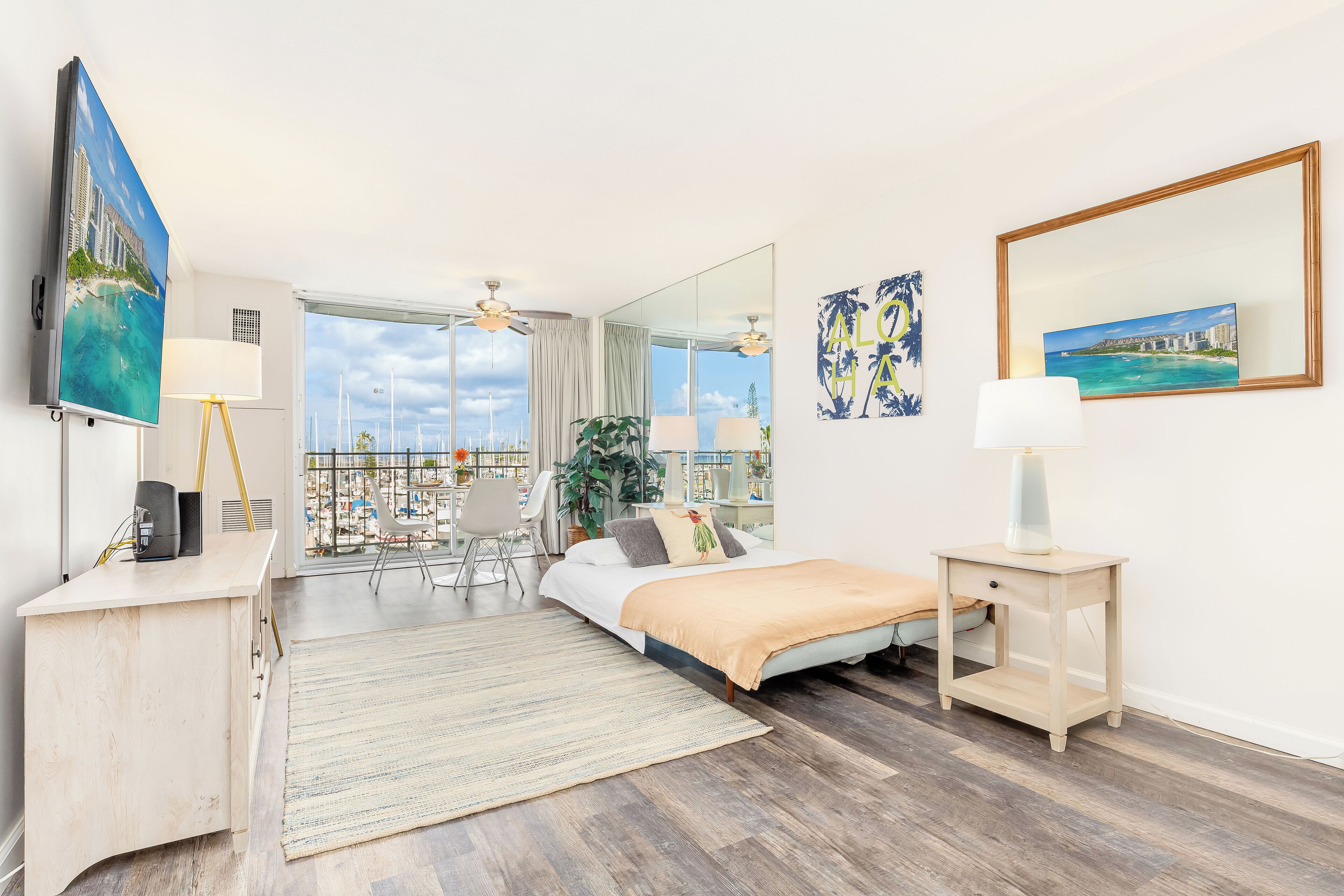 Ein Hotelzimmer mit Bett, Schreibtisch, Stuhl, kleinem Tisch, Lampe, Spiegel und Blick auf die Stadt.