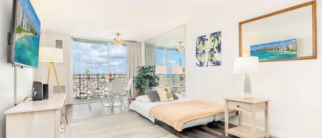 Ein Hotelzimmer mit Bett, Schreibtisch, Stuhl, kleinem Tisch, Lampe, Spiegel und Blick auf die Stadt.