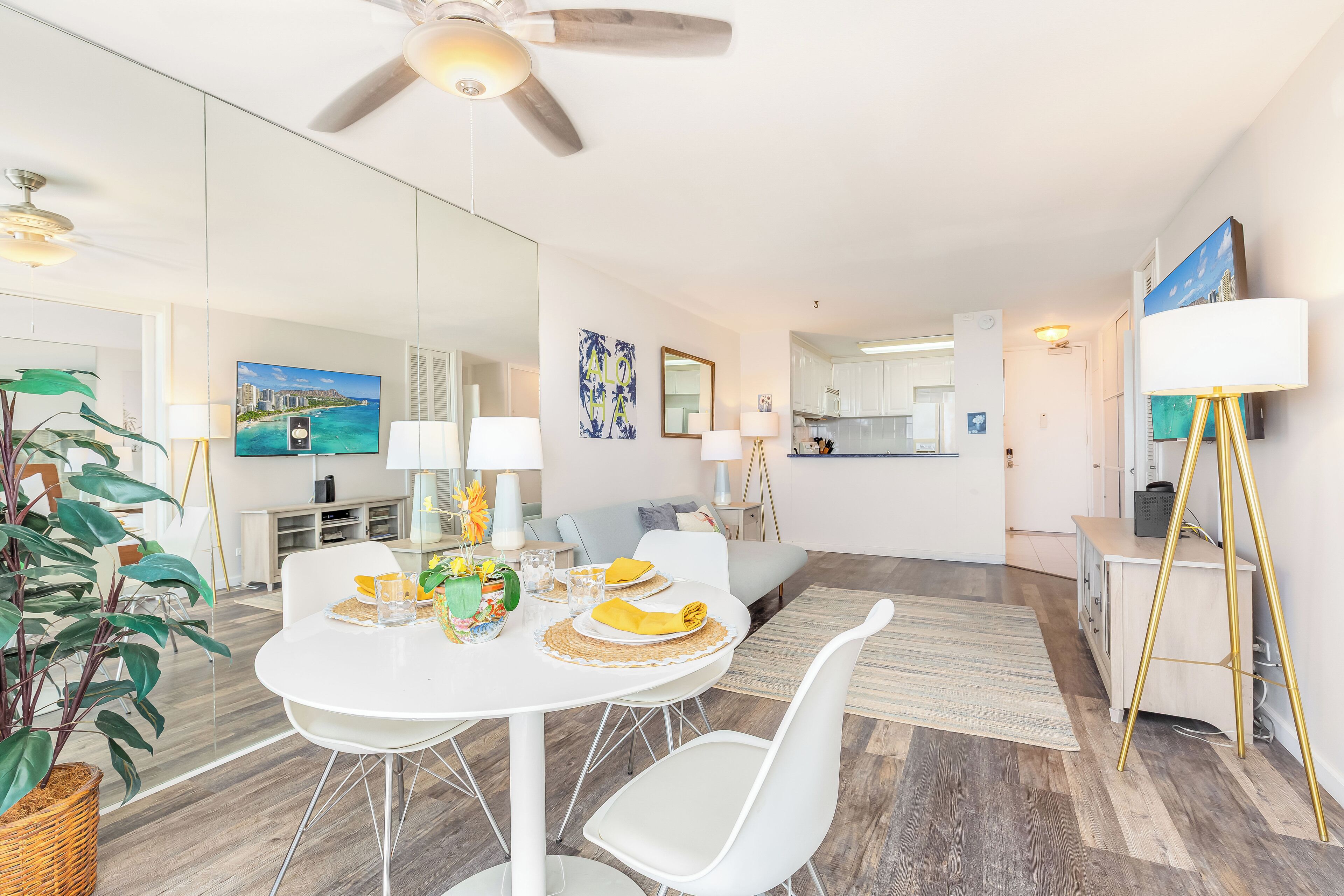 A modern living room with a dining area, a kitchen, and a large mirror reflecting the space.