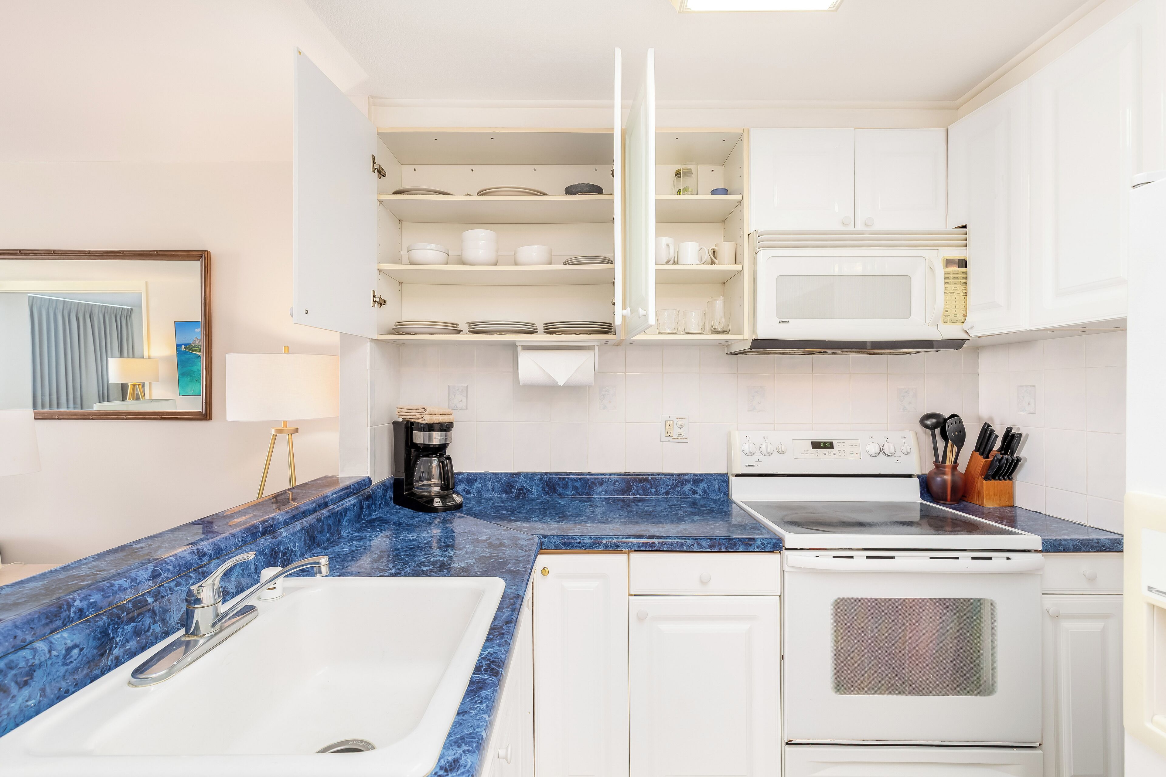 A modern kitchen with white cabinets, a blue marble countertop, a built-in microwave, and a stove.