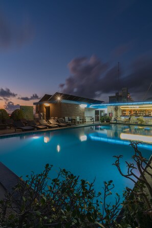 A swimming pool with lounge chairs, a bar area, and a building with a brick facade.