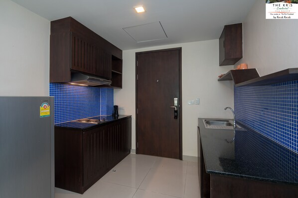 A compact kitchen with dark wood cabinets, a blue tiled backsplash, and a stainless steel sink.
