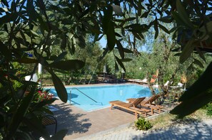 Piscina con sillas de descanso y sombrilla, rodeada de follaje.