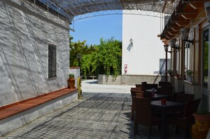 Un área de patio al aire libre con piso de piedra, mobiliario de mimbre y plantas en macetas.