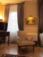 Una sala de estar con una televisión sobre una mesa de madera, un sillón color beige, un radiador y un cuadro en la pared.