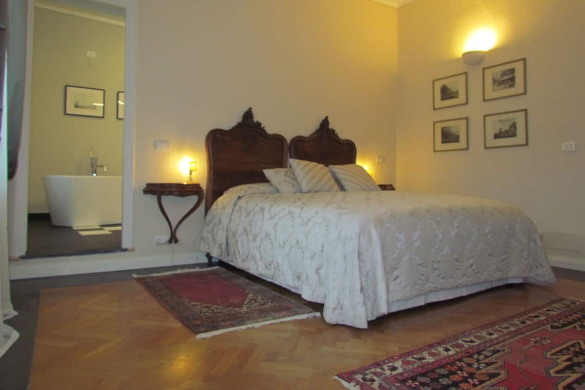 Ein Schlafzimmer mit einem großen Bett, einem Holzkopfstück, einem Nachttisch, einer wandmontierten Lampe und einem durch eine offene Tür einsehbaren Badezimmer.