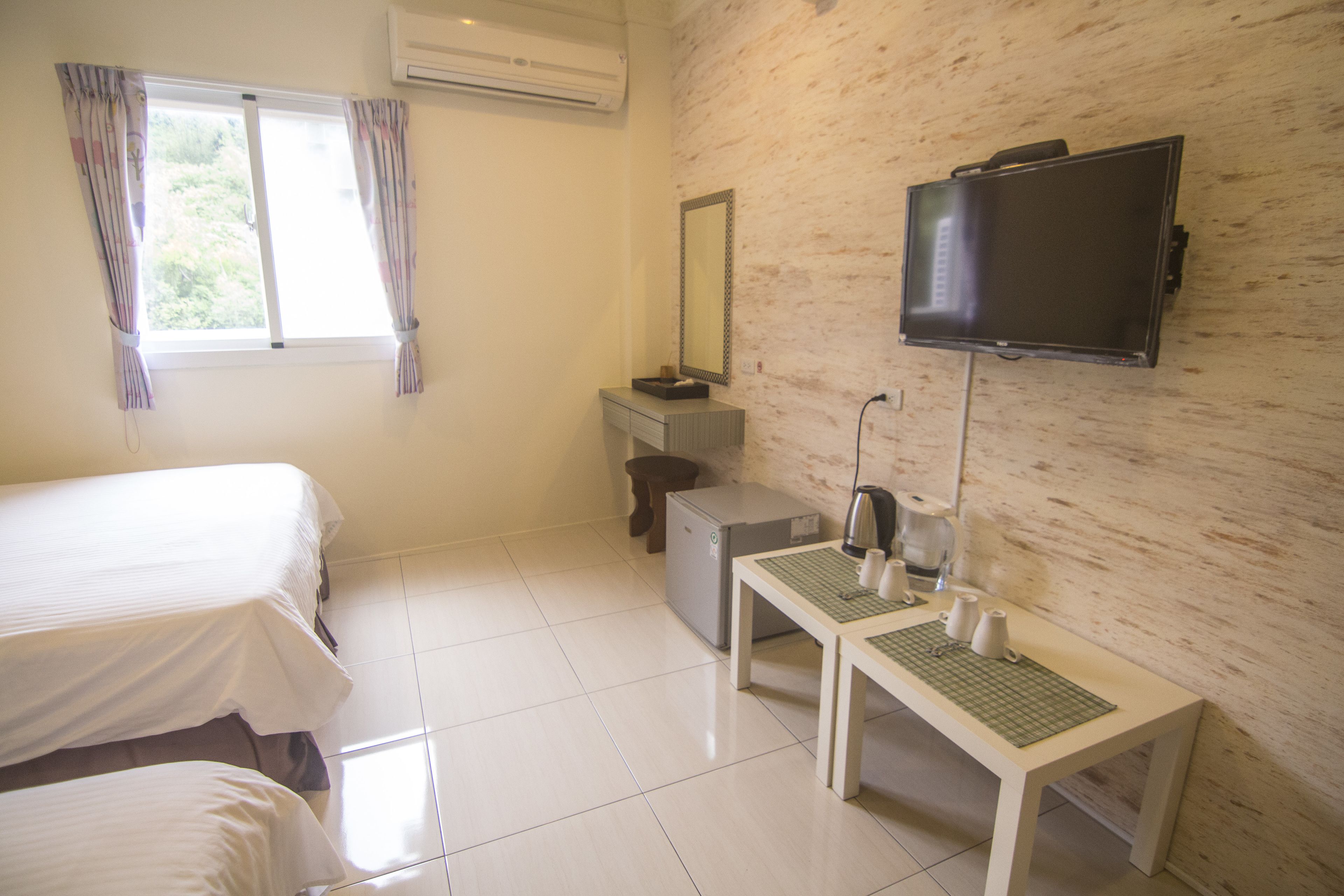 Un dormitorio con dos camas, un escritorio con espejo, una televisión y una ventana con cortinas.