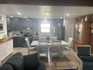 A compact kitchen with dark cabinets, a microwave, stove, and refrigerator. There is a dining area with a table and chairs. - Amazing Gulf Views, Pets Welcomed ADA Ramp, Fenced Yard, Direct access to Beach (Galveston)
