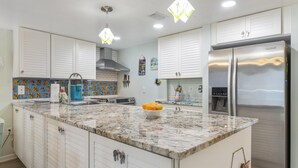 Una cocina con armarios blancos, un refrigerador de acero inoxidable, encimera de mármol y un lavamanos.