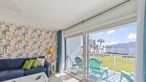 Una habitación con un sofá azul, una mesa de centro blanca y vistas a un césped verde con sillas afuera.