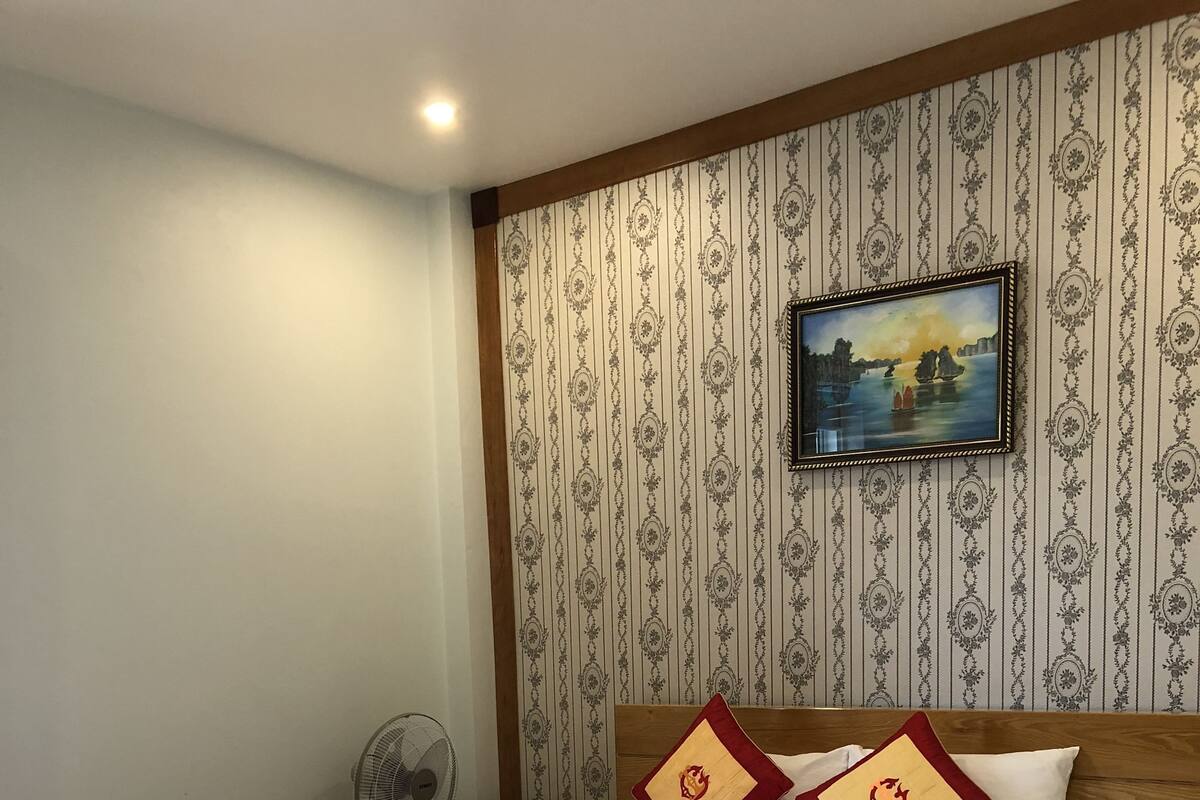 A neatly made bed with a wooden frame, a patterned wallpaper, and a framed picture on the wall.