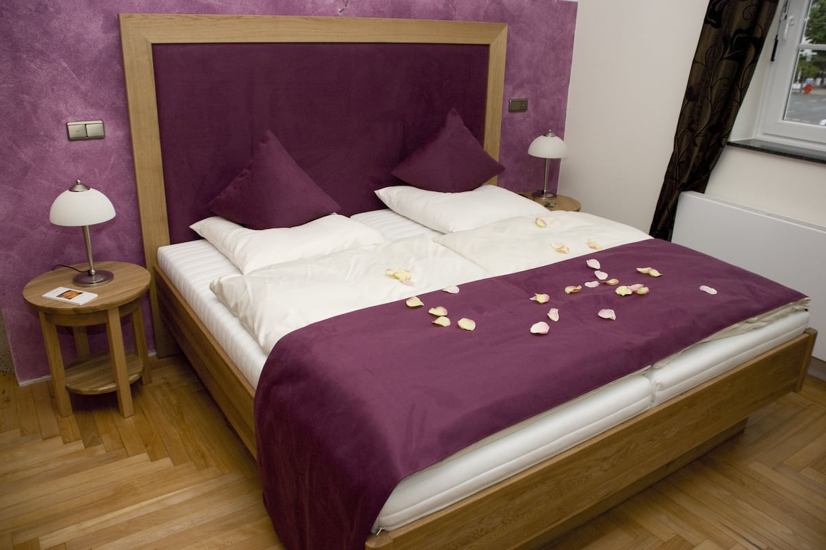 A neatly made bed with a purple bedspread and white linens, two bedside tables with lamps, and a wooden headboard.