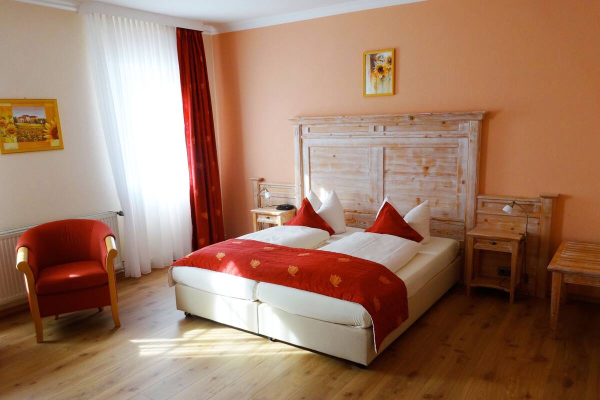 A bedroom with a bed, a chair, a nightstand, a lamp, and a painting on the wall.