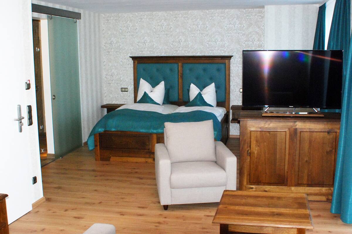 A bedroom with a bed, a TV, a chair, and a wooden cabinet.