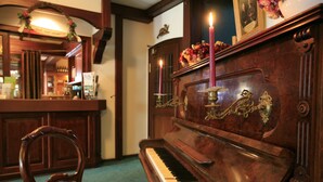 A wooden piano with a decorative plaque and two lit candles, a wooden chair, and a bar area with a mirror and framed pictures. - Rüter's Hotel & Restaurant (Salzhausen)