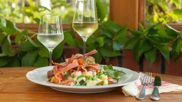 A plate of food with bacon, greens, and a glass of white wine on a wooden table.