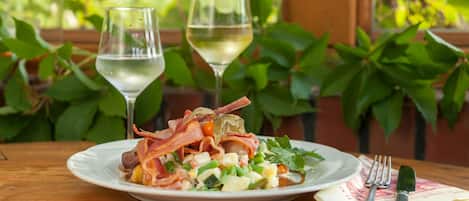 A plate of food with bacon, greens, and a glass of white wine on a wooden table.
