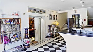 A modern hotel lobby with a checkered floor, a reception desk, a coffee machine, and a display of magazines and books. - San Valentino (Rome)