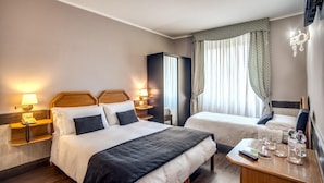 Une chambre d’hôtel avec deux lits, une table de chevet en bois avec une lampe, une petite table avec une télécommande et des verres, et un téléviseur fixé au mur.