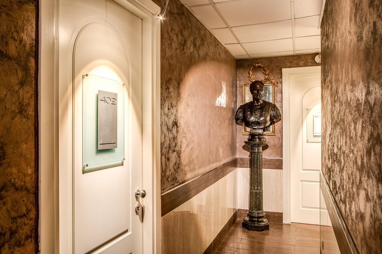 Um corredor com parede de mármore, uma porta com placa de número e uma estátua.