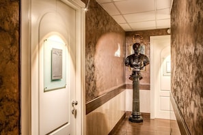 A hallway with a marble wall, a door with a number plate, and a statue. - San Valentino (Rome)