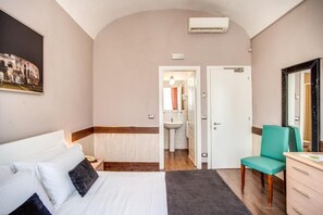 A hotel room with a bed, a desk, a chair, a mirror, and a bathroom visible through an open door. - San Valentino (Rome)