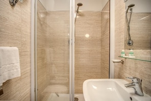 A modern bathroom with a glass-enclosed shower, a white sink, and a glass shelf with toiletries. - San Valentino (Rome)