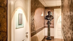 A hallway with a marble wall, a door with a number plate, and a statue. - San Valentino (Rome)