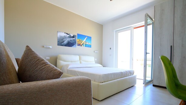A modern bedroom with a bed, a sofa, and a green chair. There are two paintings on the wall.